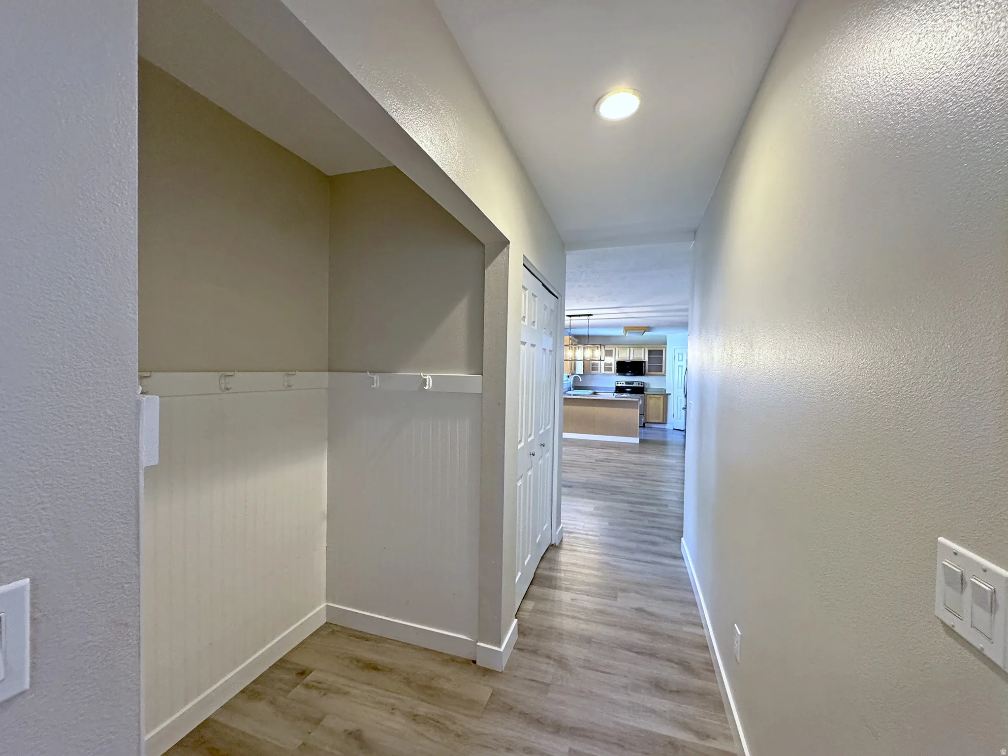 Hallway with wood-finish flooring, recessed lighting, and a built-in storage alcove featuring beadboard paneling