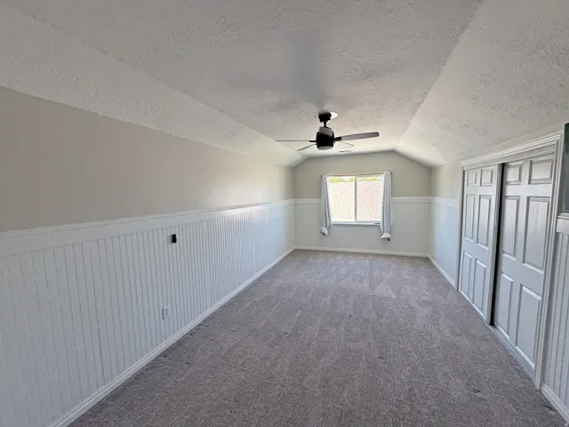 Carpeted room featuring a sloped ceiling, wainscoting, a window with blinds, and a ceiling fan