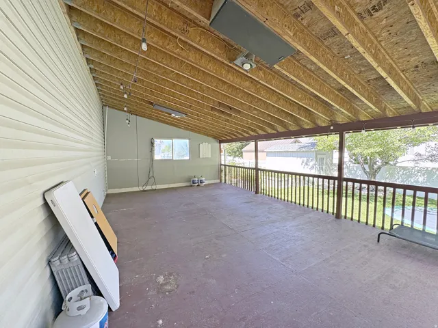 Covered exterior patio featuring a wood railing and exposed rafter ceiling