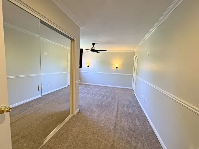 Mirrored sliding doors, crown molding, wall sconces, ceiling fan, and carpeted flooring