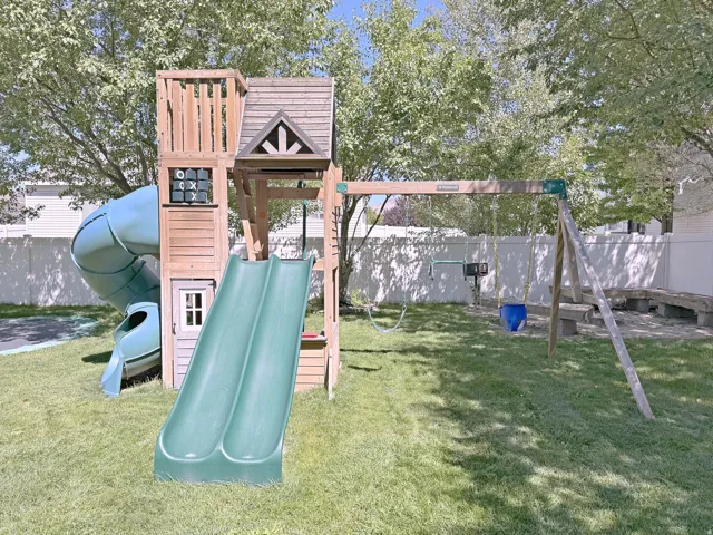 Expansive backyard with a manicured lawn, a wooden playset featuring two slides and a spiral slide, and a swing set