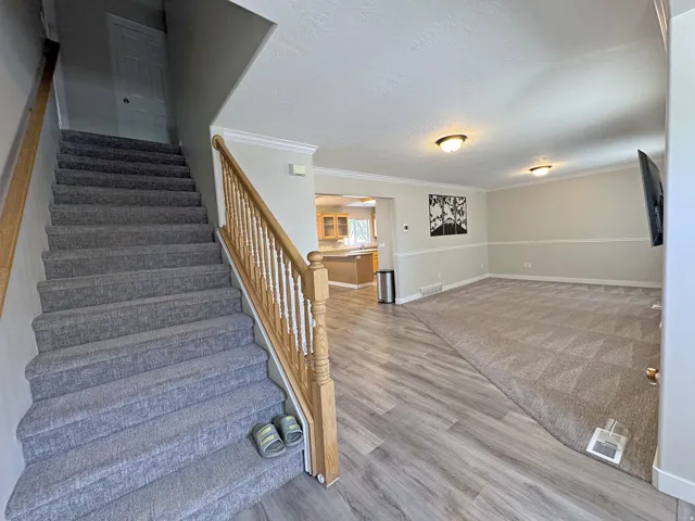 Carpeted staircase with wood banister, wood-finish flooring, recessed lighting, and crown molding