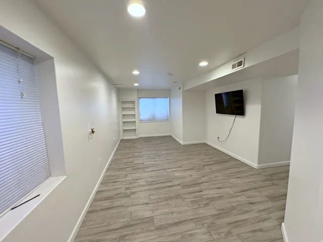 Recessed lighting illuminates the wood-finish flooring in this space featuring a built-in shelving unit and window treatments