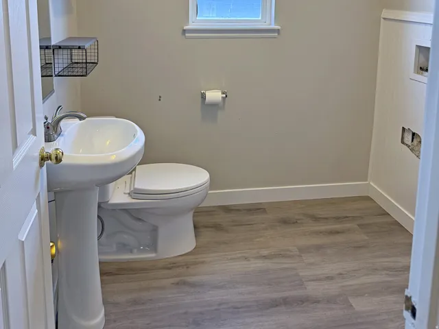 Pedestal sink, wall-mounted shelving, and wood-finish flooring