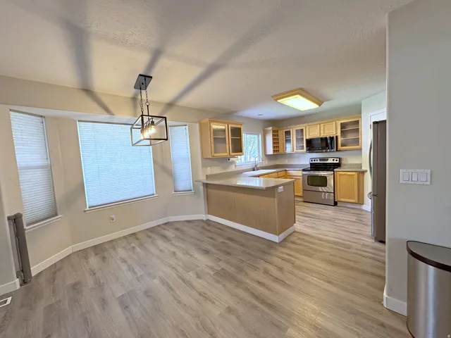 Kitchen with wood-finish flooring, light wood cabinetry, stainless steel appliances, and a peninsula with countertop seating