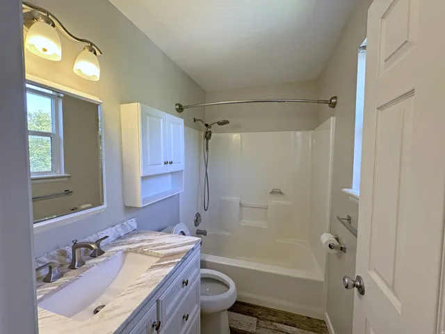 Bathroom featuring a single vanity with a patterned countertop, a built-in medicine cabinet, and a shower-tub combination with a curved shower rod