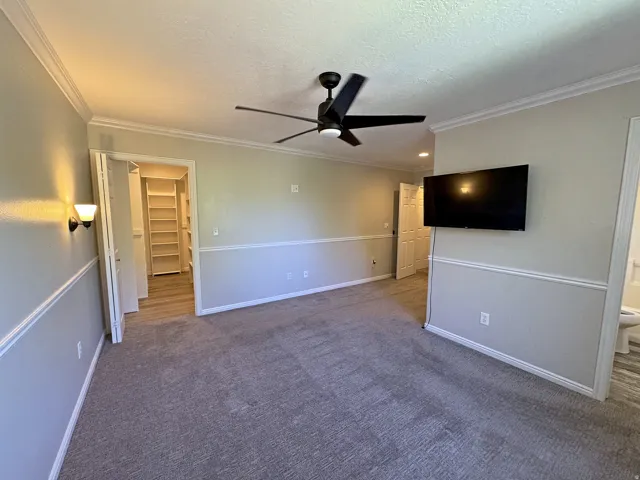 Ceiling fan with integrated lighting, wall sconce, crown molding, chair rail molding, and a built-in closet system