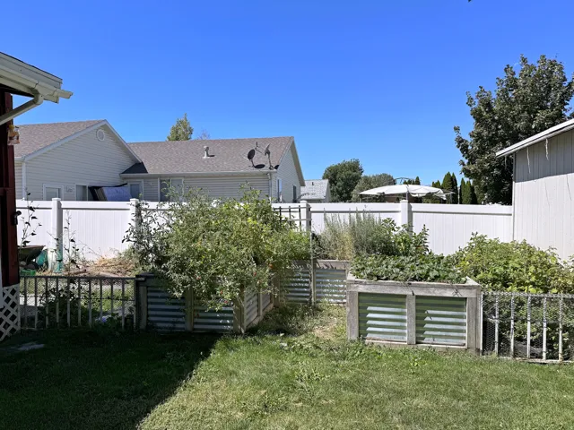 Backyard with raised garden beds, a white privacy fence, and grass landscaping