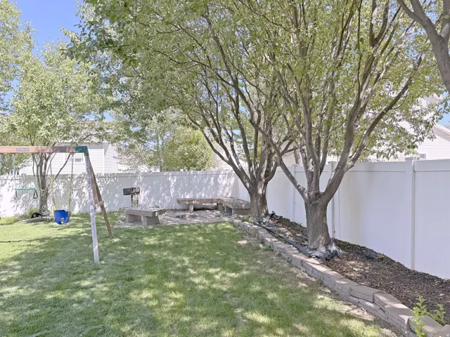 Expansive backyard featuring a privacy fence, established trees, and a built-in fire pit with stone benches