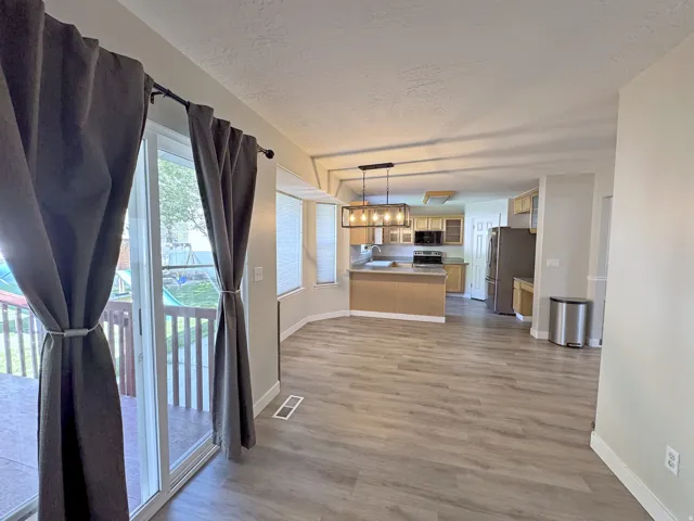 Open-concept living area with wood-finish flooring, a sliding glass door leading to an outdoor deck, and a kitchen featuring stainless steel appliances and pendant lighting
