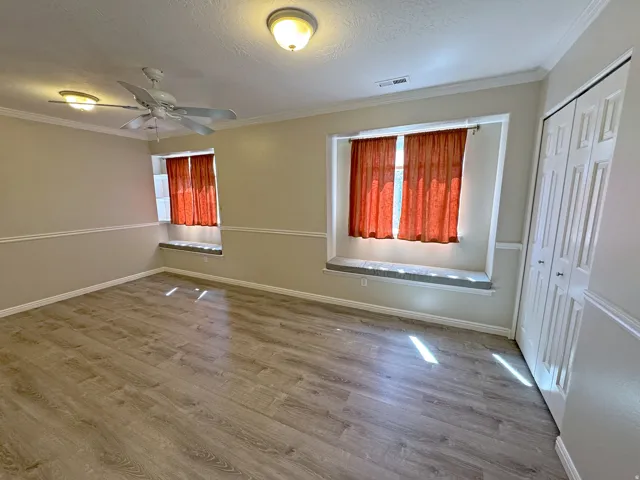 Light-toned wood-finish flooring, two ceiling-mounted light fixtures, a ceiling fan, and built-in closet storage