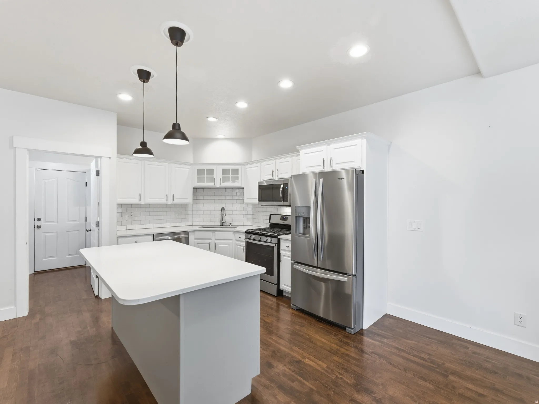 White shaker cabinetry, stainless steel appliances, white subway tile backsplash, wood-finish flooring, and a central island with pendant lighting