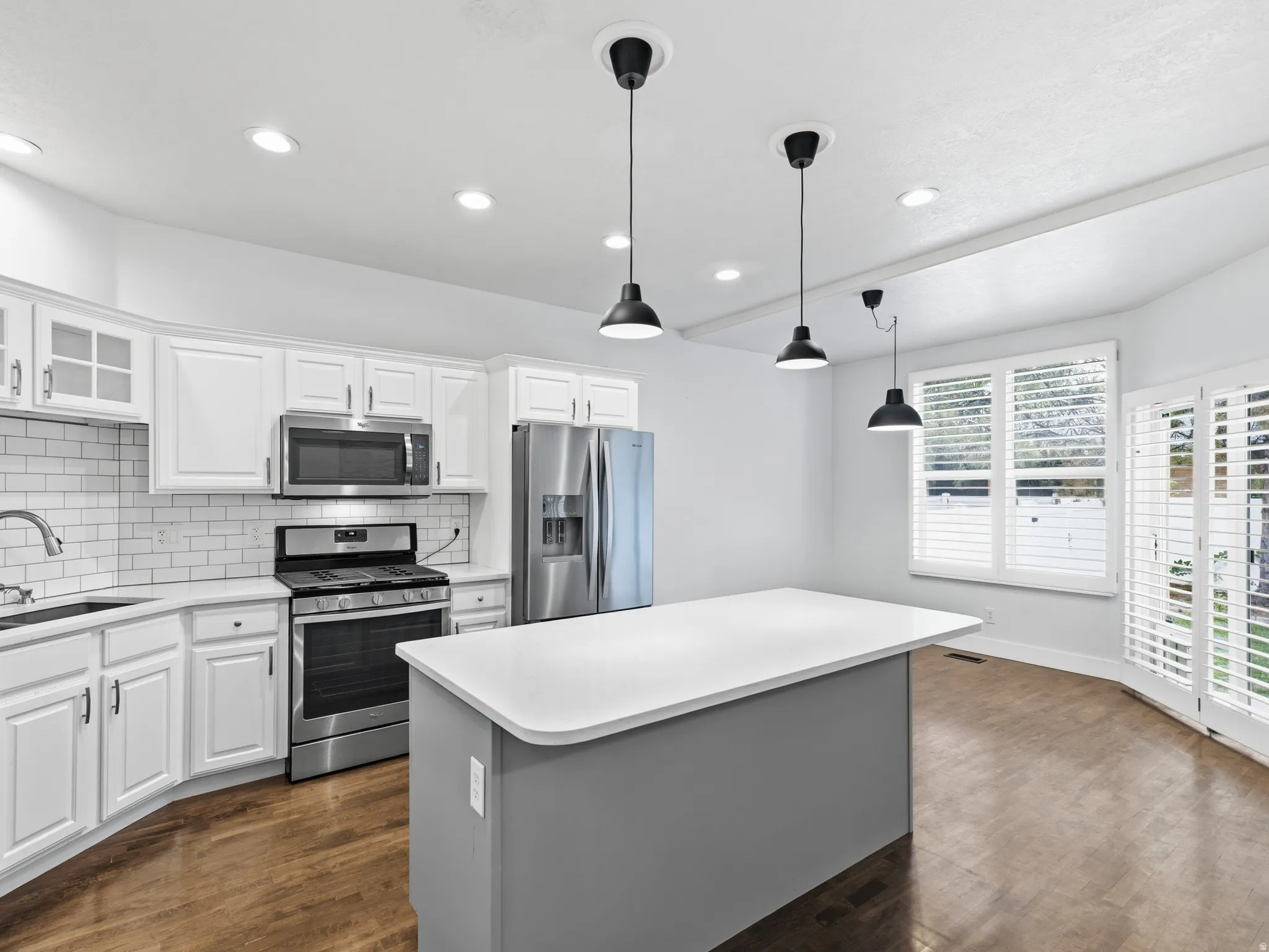 Kitchen featuring wood-finish flooring, white cabinetry, stainless steel appliances, a center island with a solid surface countertop, and recessed lighting