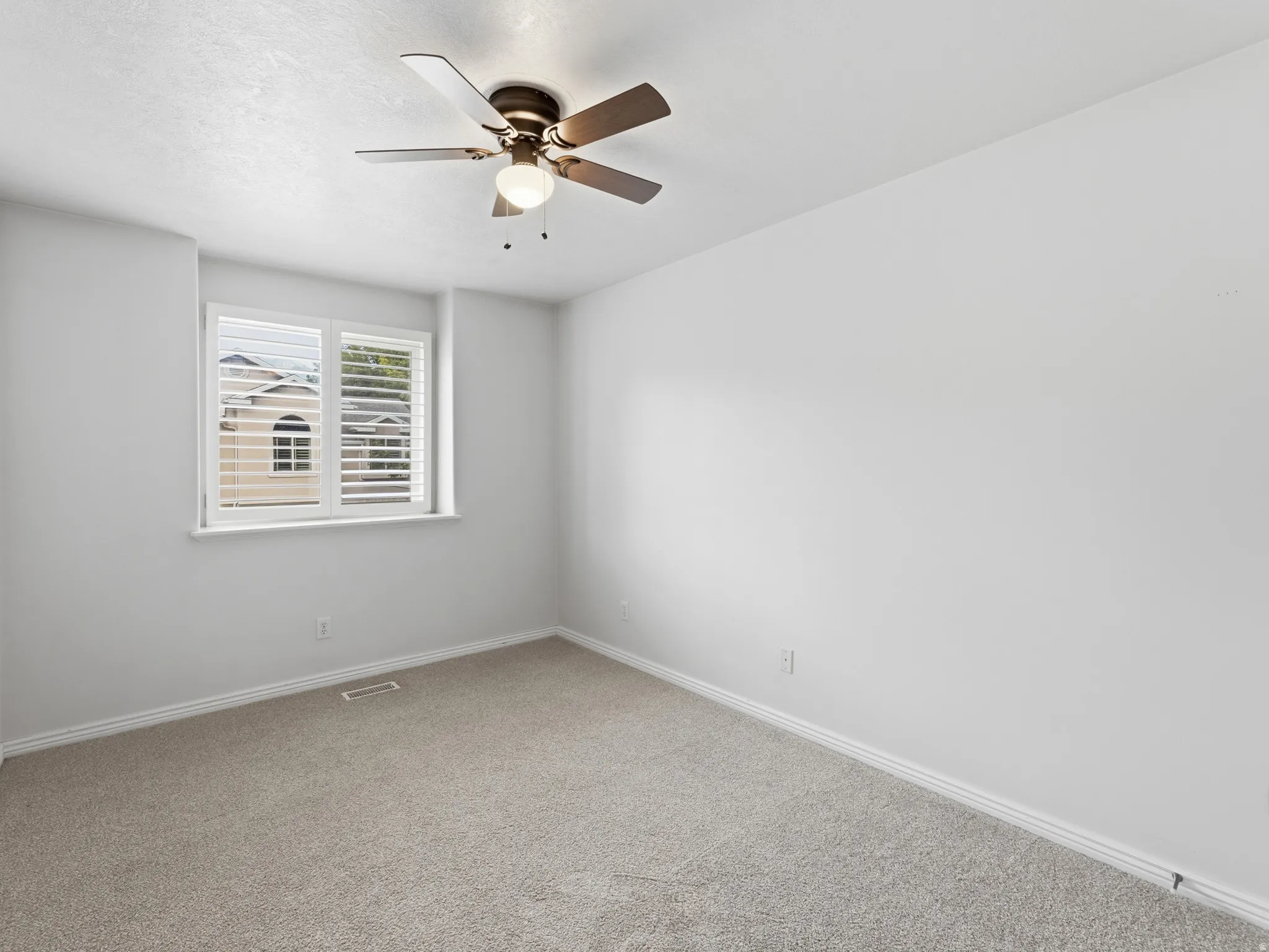 Neutral wall finishes, recessed window with white plantation shutters, textured carpet flooring, and a ceiling fan with integrated lighting