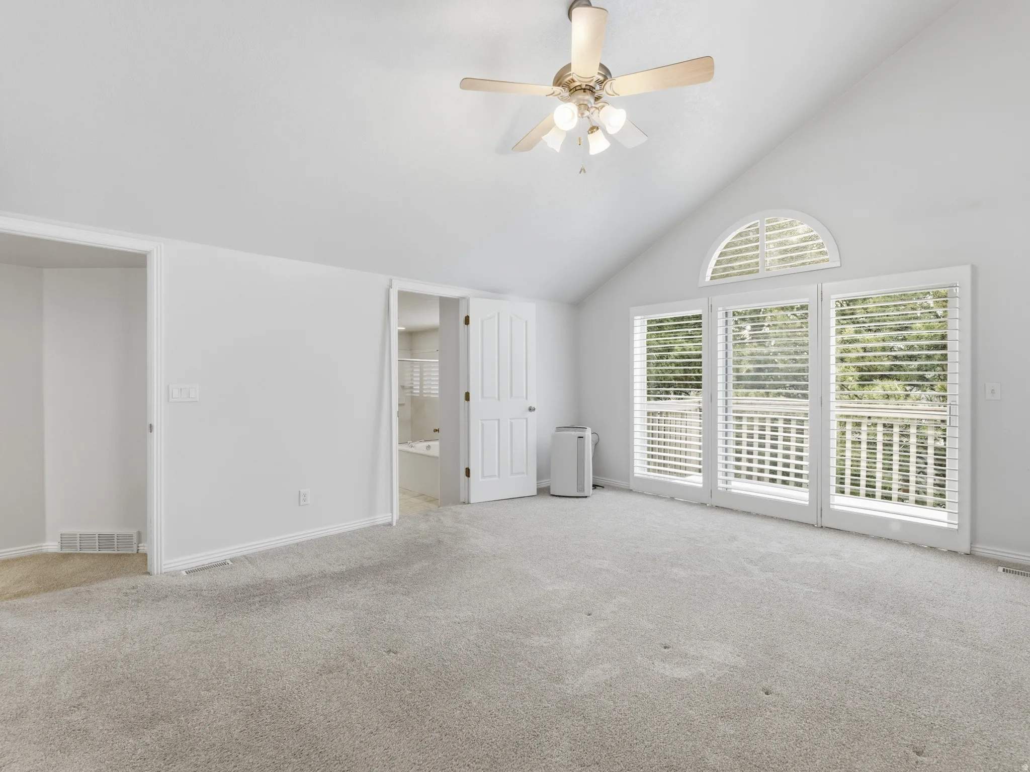 Vaulted ceiling with a ceiling fan, light gray carpet, multiple white-framed windows with blinds, and white interior doors