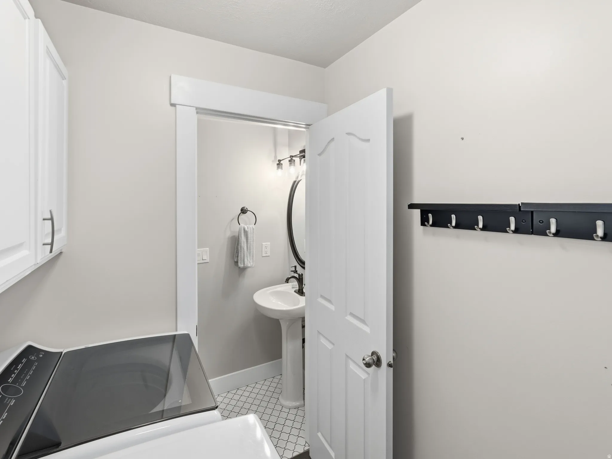 White upper cabinetry with brushed nickel pulls, white interior door, and wall-mounted coat rack