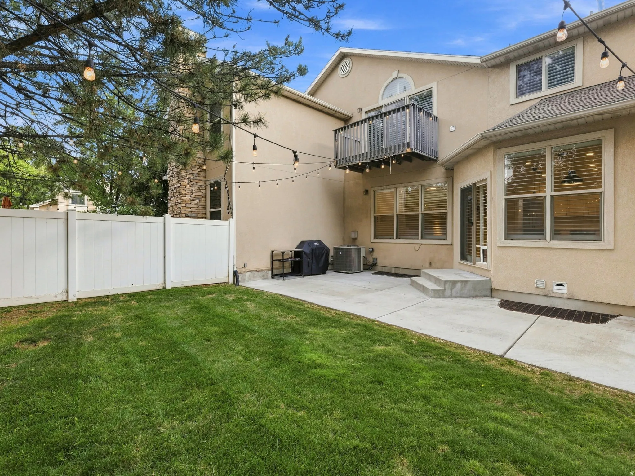Stucco exterior with a stone chimney accent, featuring a private balcony, concrete patio, and a white privacy fence enclosing a grass yard