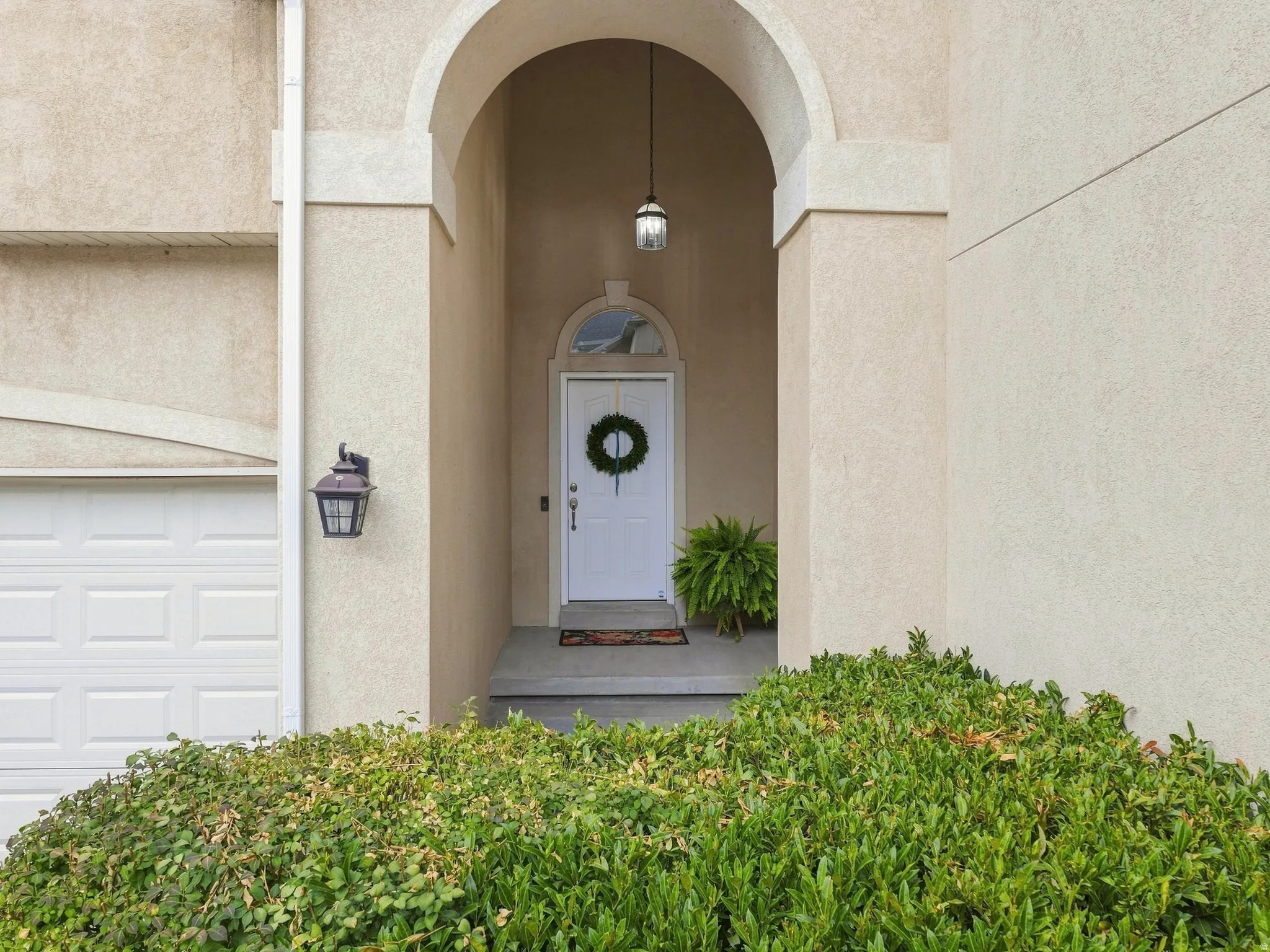 Arched entry with a white paneled door, exterior wall lantern, and a stucco finish