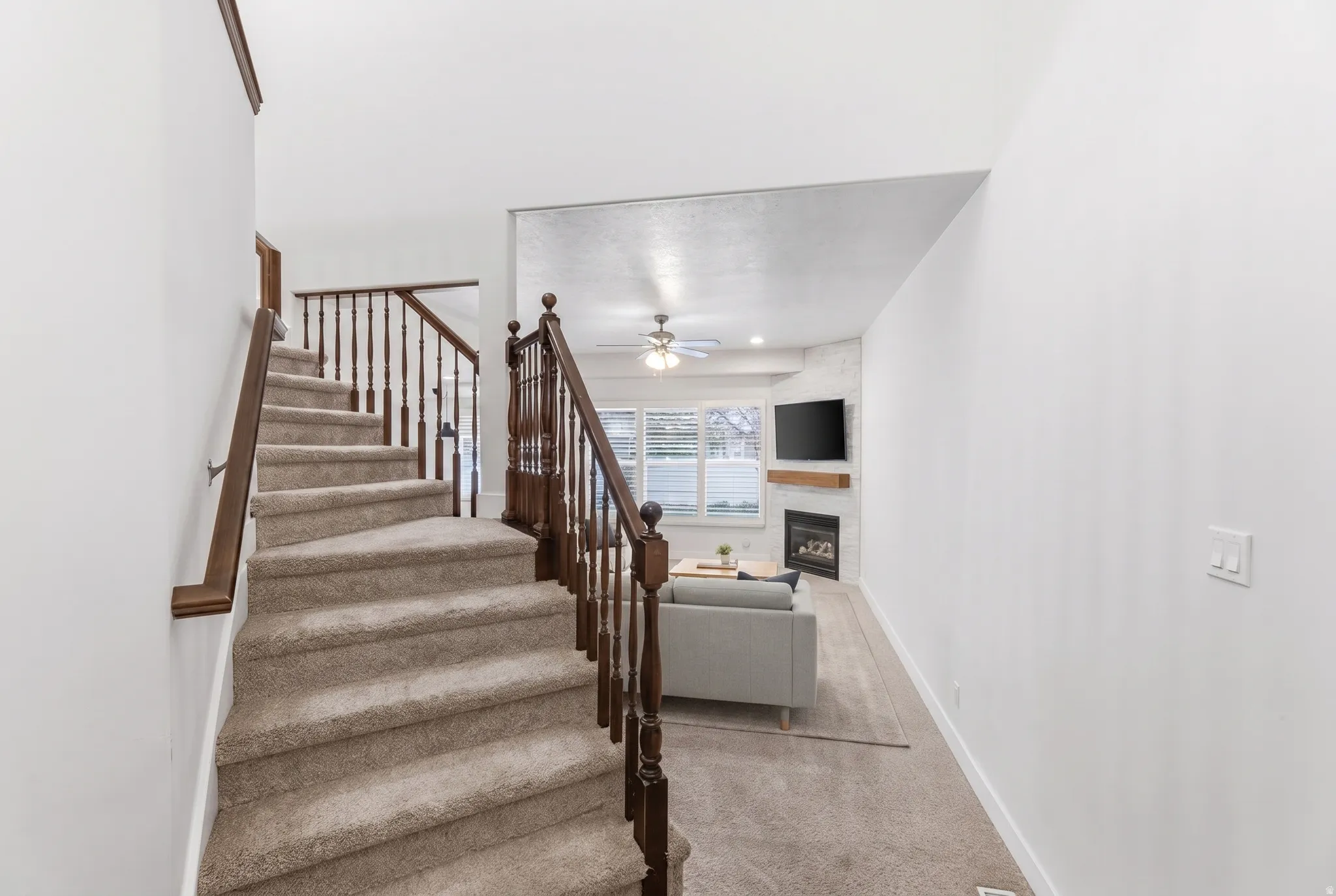 Carpeted staircase with wood railing and balusters, featuring a living area with a fireplace, mantel, and a ceiling fan