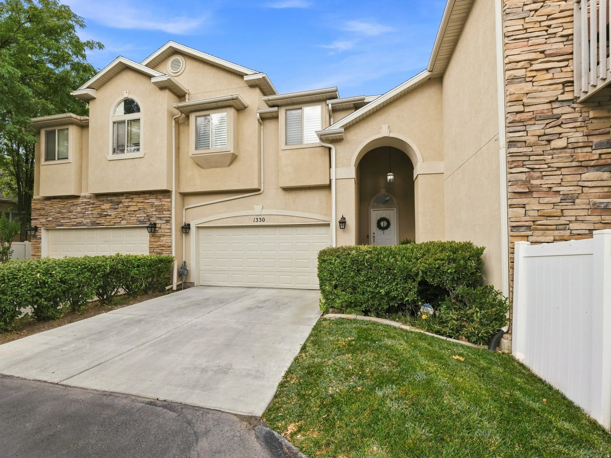 Stucco exterior with stone accents, arched entryway, attached garage, concrete driveway, and manicured landscaping