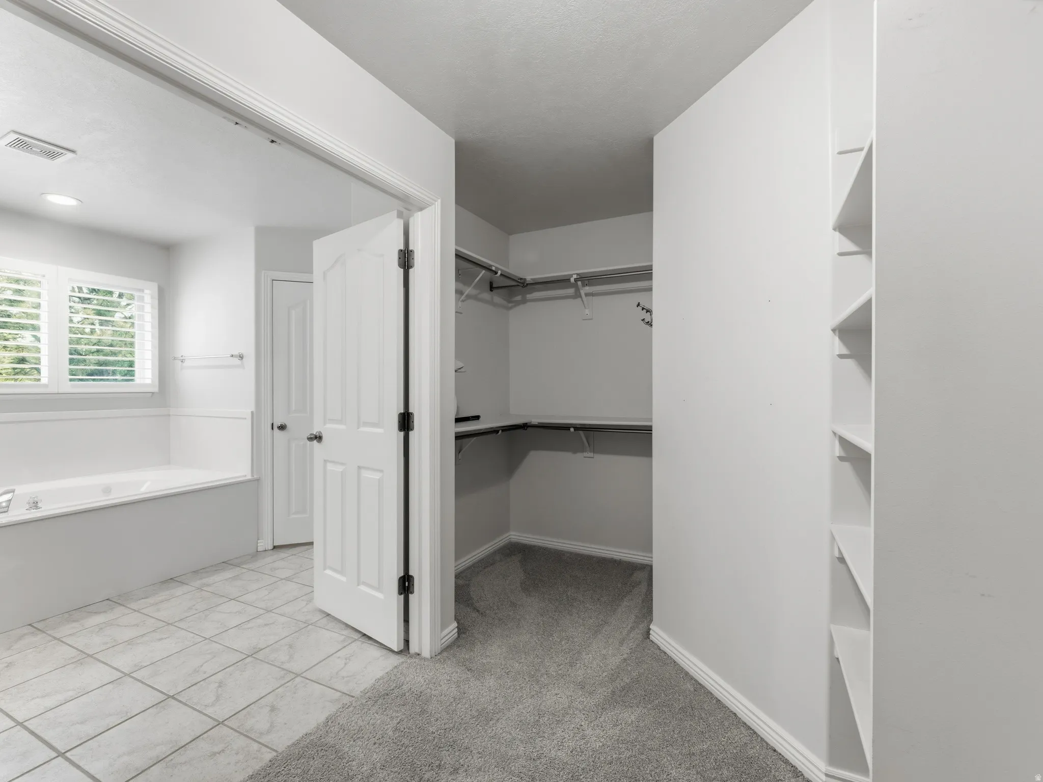 Primary Bathroom and Walk-In Closet featuring ceramic tile flooring, dual vanity with ample counter space, large mirror with integrated lighting, white cabinetry, and an expansive closet with built-in shelving and hanging rods throughout