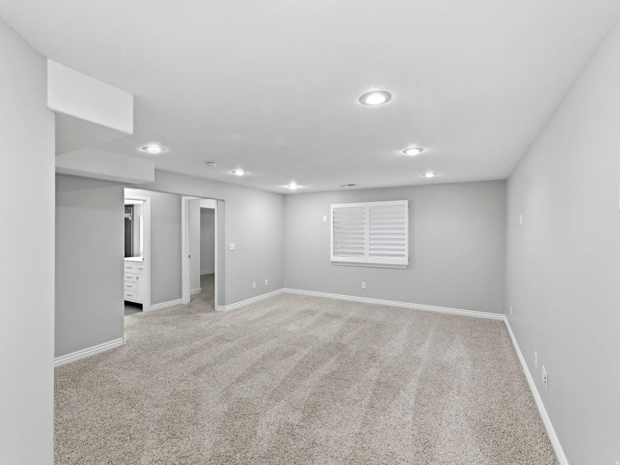 Recessed lighting, light gray wall paint, window with white plantation shutters, gray carpet flooring, and white trim