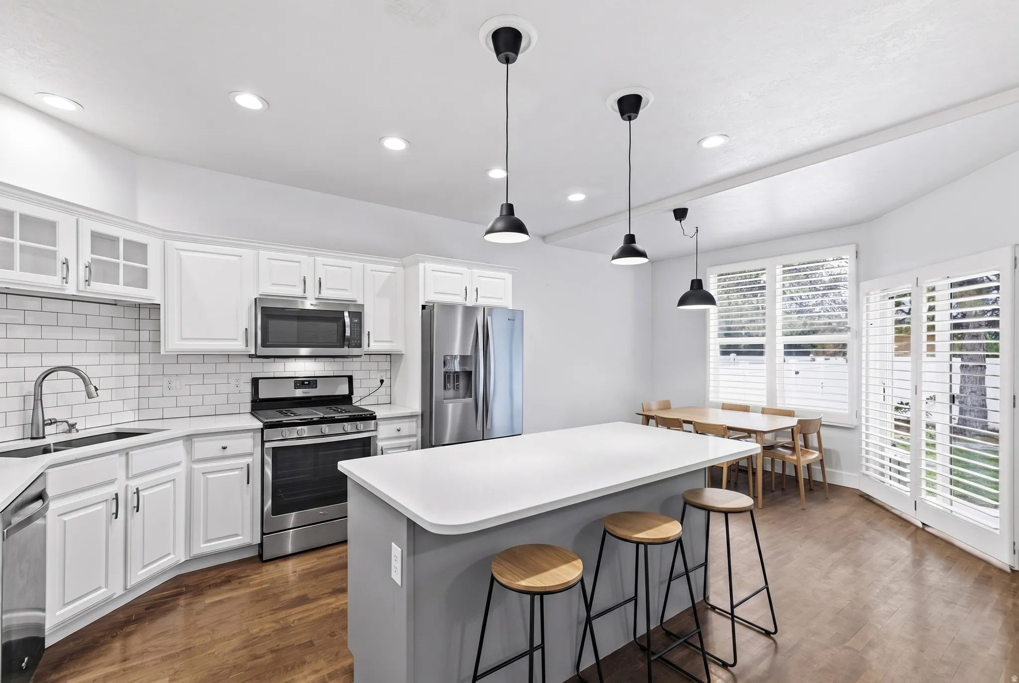 White cabinetry, stainless steel appliances, white subway tile backsplash, a center island with countertop seating, and wood-finish flooring