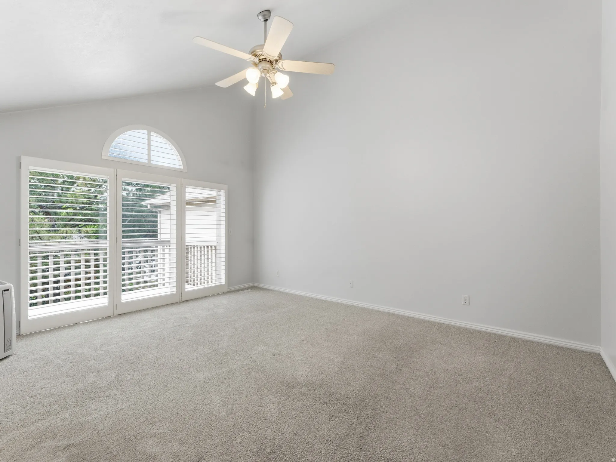 Vaulted ceiling with a ceiling fan, light-colored carpet, white walls, and a glass door with a transom window