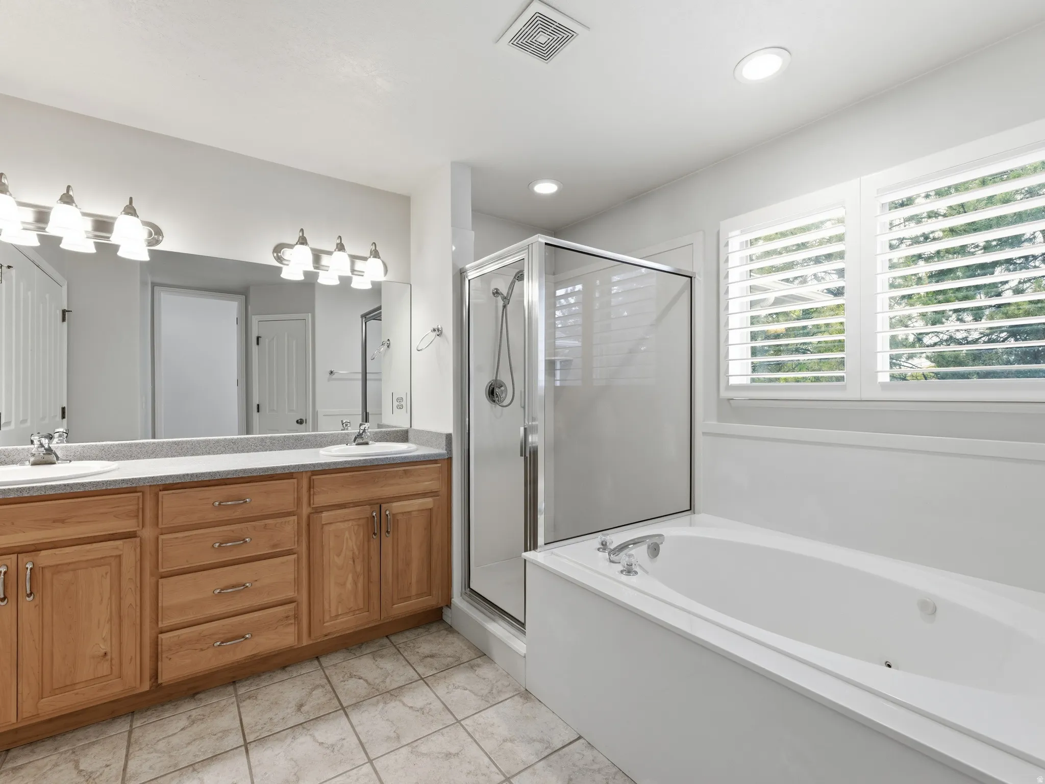 Dual vanity with light wood cabinetry, stone-finish countertop, and undermount sinks