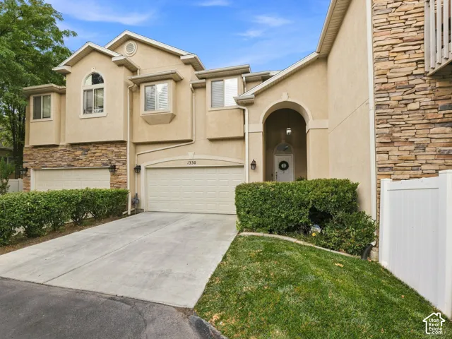 Stucco exterior with stone accents, arched entryway, attached garage, concrete driveway, and manicured landscaping