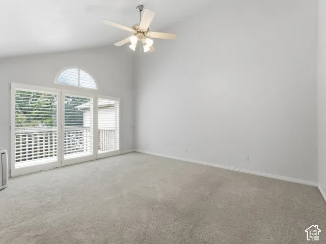 Vaulted ceiling with a ceiling fan, light-colored carpet, white walls, and a glass door with a transom window