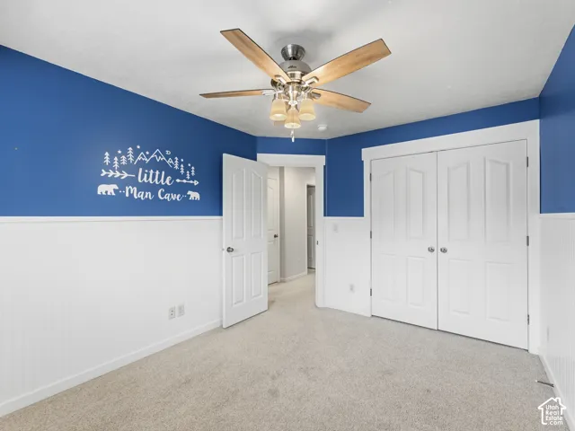 White beadboard wainscoting, light carpet flooring, ceiling fan with light fixture, and white bi-fold closet doors
