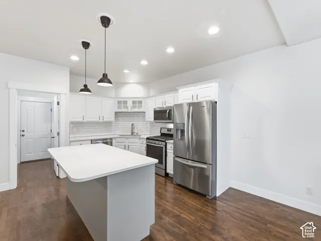 White shaker cabinetry, stainless steel appliances, white subway tile backsplash, wood-finish flooring, and a central island with pendant lighting