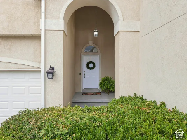 Arched entry with a white paneled door, exterior wall lantern, and a stucco finish