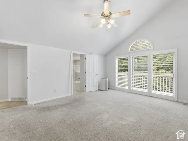 Vaulted ceiling with a ceiling fan, light gray carpet, multiple white-framed windows with blinds, and white interior doors