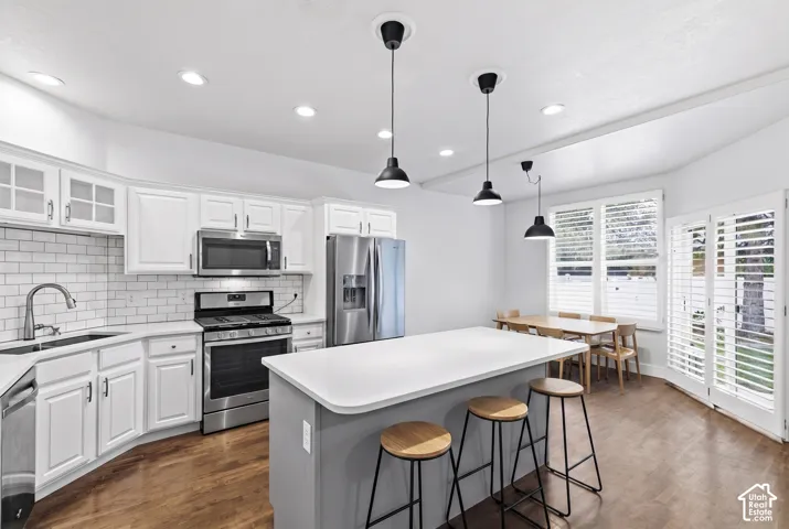 White cabinetry, stainless steel appliances, white subway tile backsplash, a center island with countertop seating, and wood-finish flooring