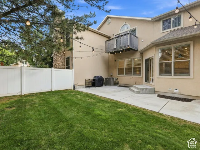 Stucco exterior with a stone chimney accent, featuring a private balcony, concrete patio, and a white privacy fence enclosing a grass yard