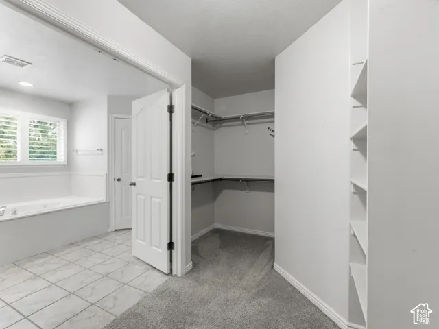 Primary Bathroom and Walk-In Closet featuring ceramic tile flooring, dual vanity with ample counter space, large mirror with integrated lighting, white cabinetry, and an expansive closet with built-in shelving and hanging rods throughout
