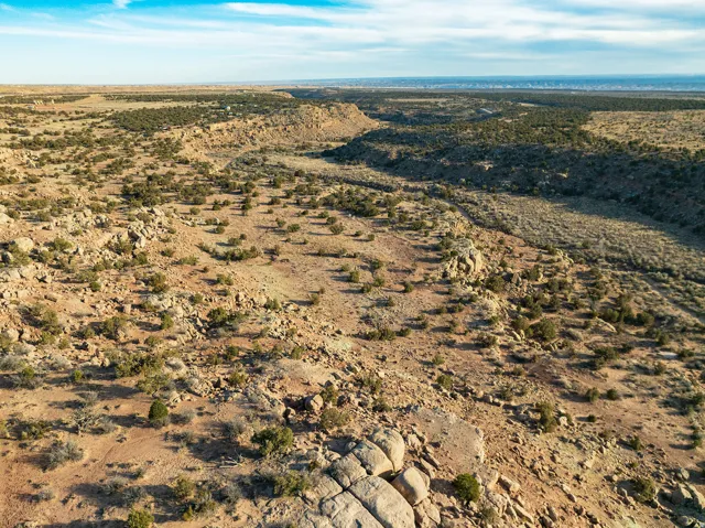 Expansive desert landscape featuring natural rock formations, scattered brush, and distant horizon