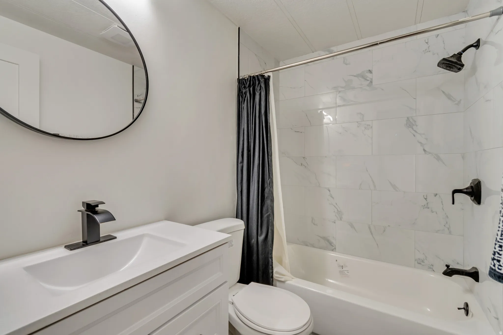 White vanity with integrated sink, black faucet, and circular mirror