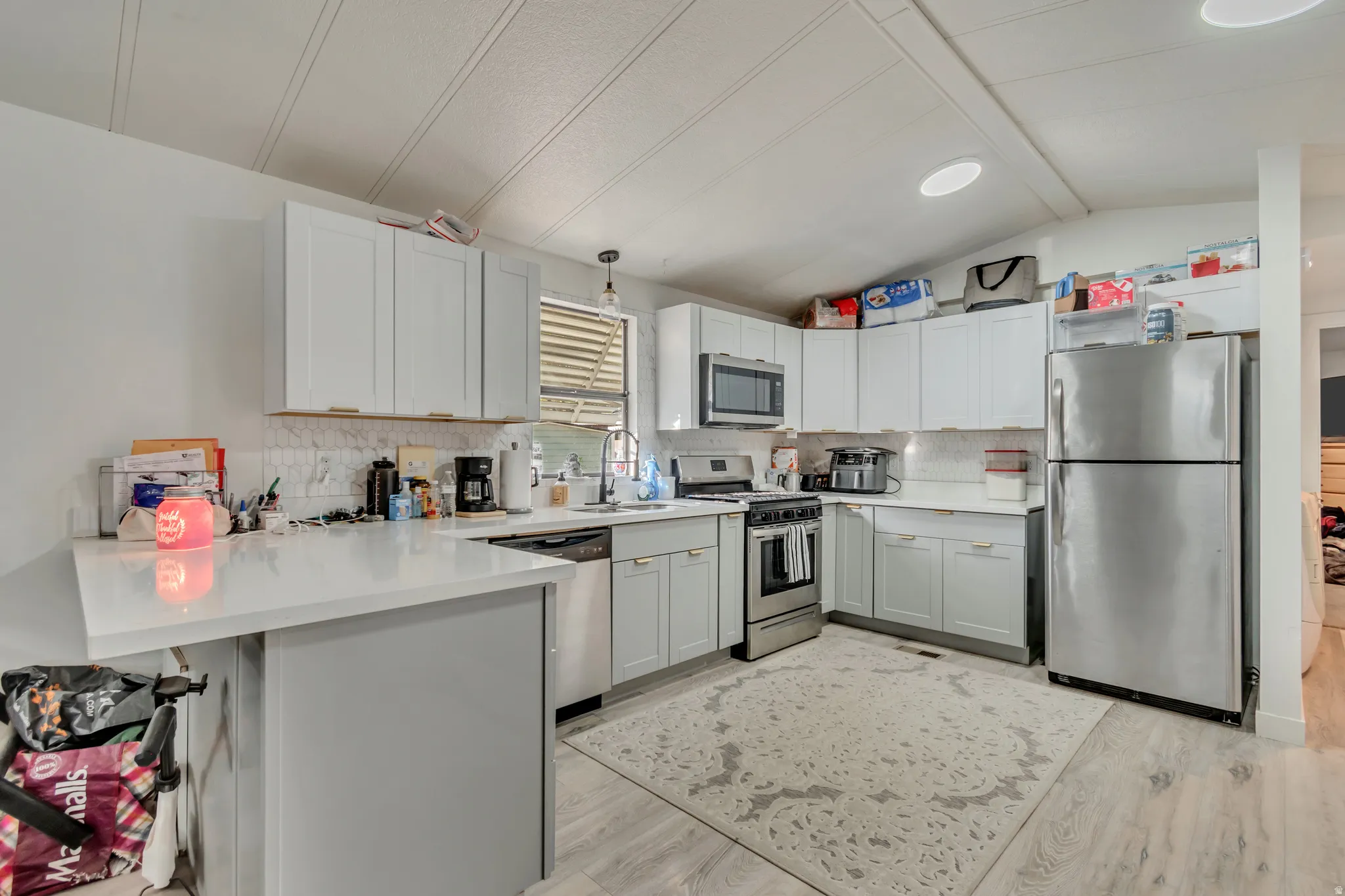 Kitchen featuring light grey cabinetry, stainless steel appliances, white countertops, and a white tile backsplash