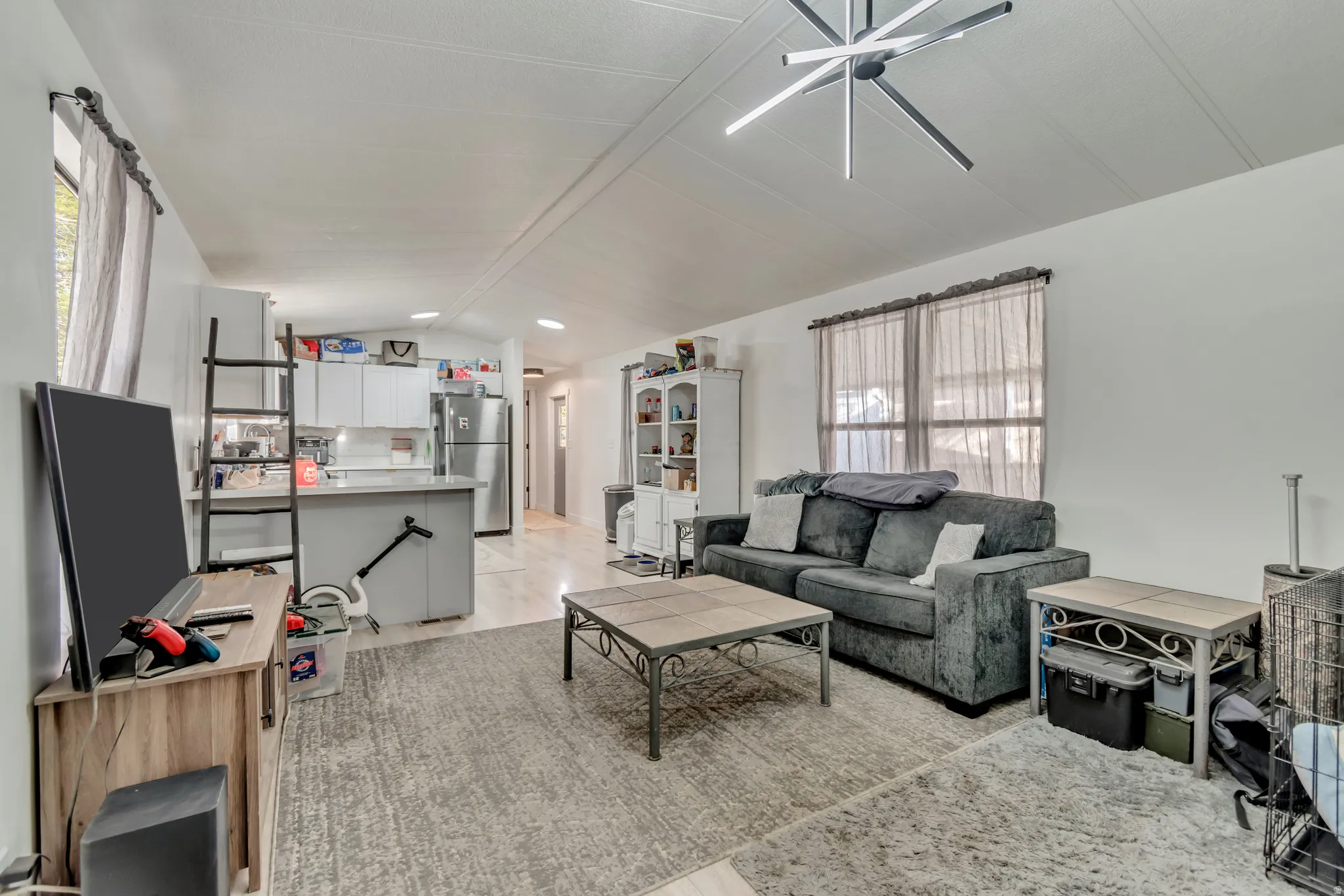 Open-concept living area featuring a modern ceiling fixture, light wood-finish flooring, and a kitchen island with seating