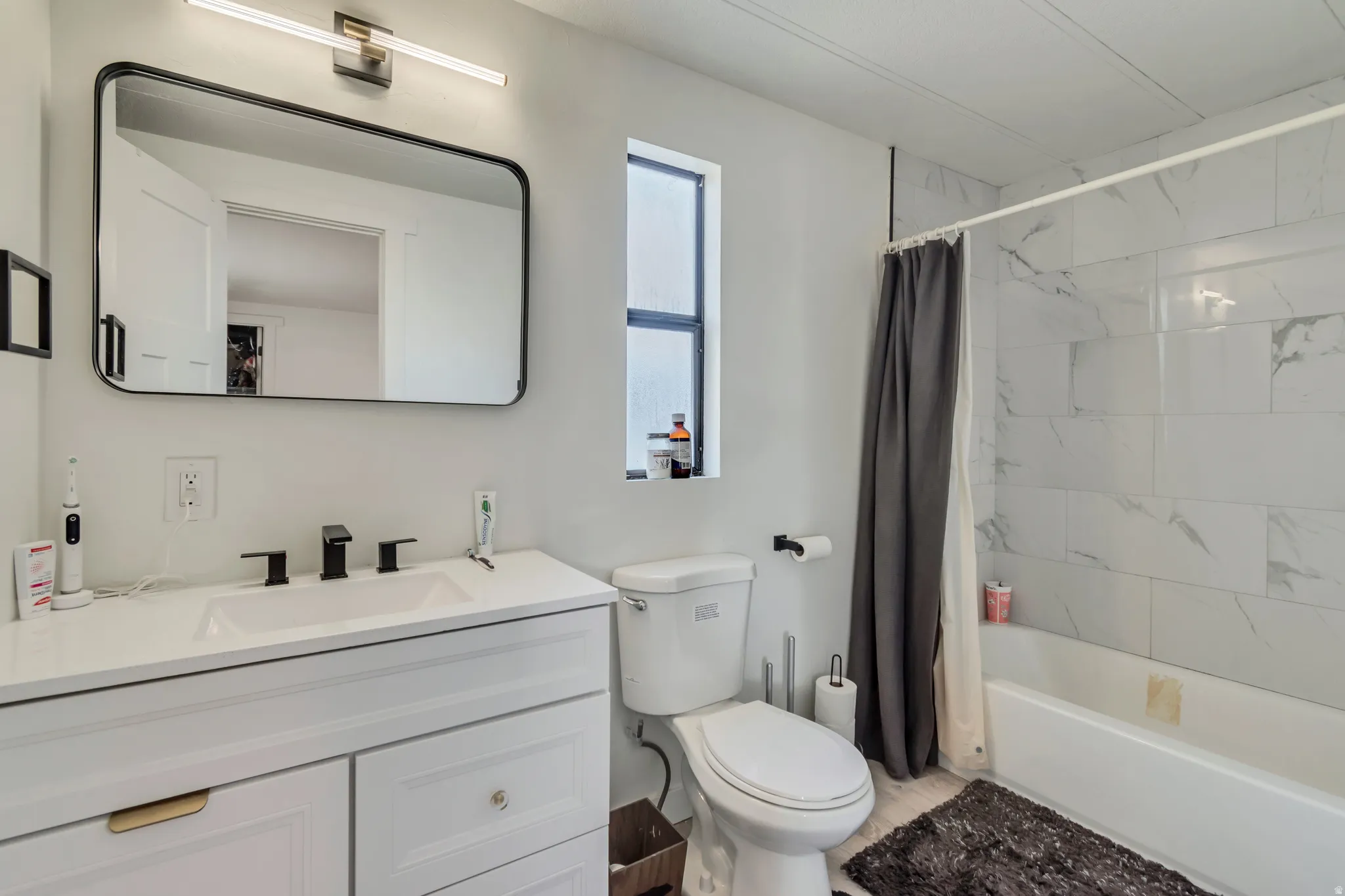 White vanity with integrated rectangular sink and matte black faucet, framed mirror, and a tiled shower-bath combination