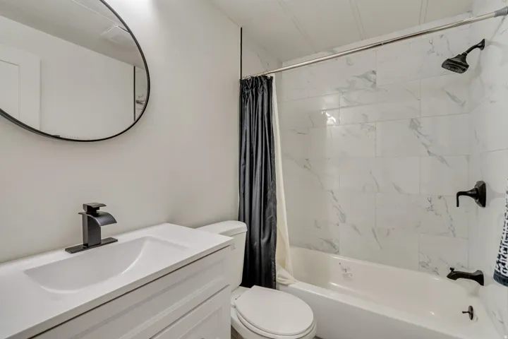 White vanity with integrated sink, black faucet, and circular mirror