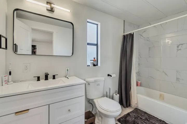 White vanity with integrated rectangular sink and matte black faucet, framed mirror, and a tiled shower-bath combination