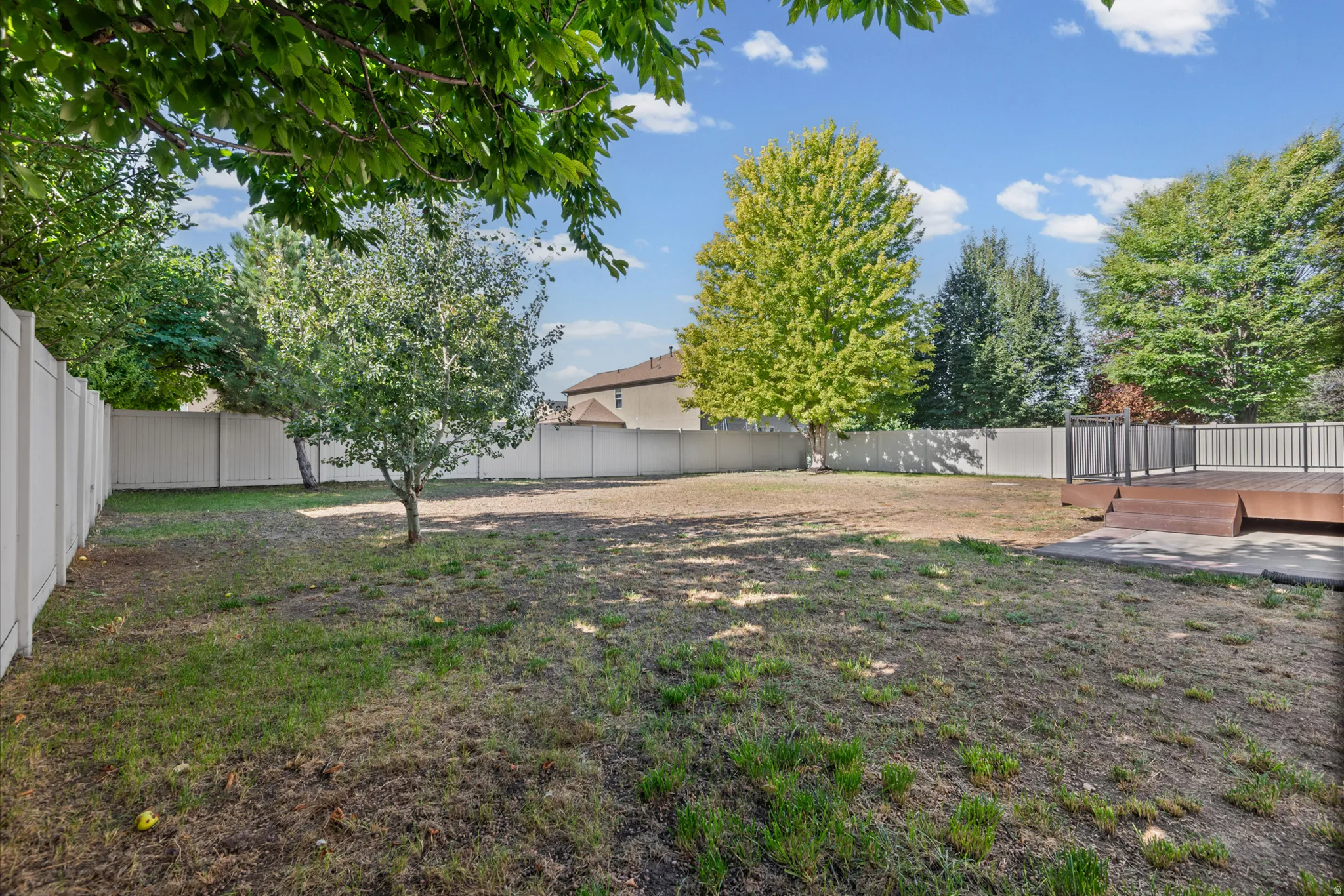 Expansive backyard featuring a privacy fence, mature trees, and a multi-level wood-finish deck with dark railings