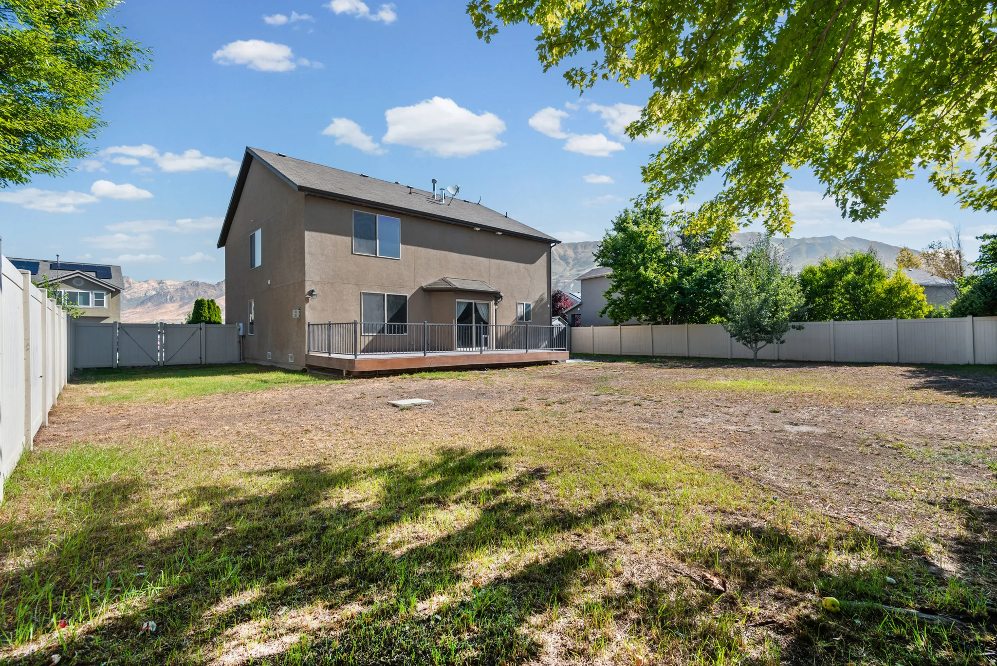 Expansive backyard with a composite deck featuring dark railings, a full-height privacy fence, and mountain scenery