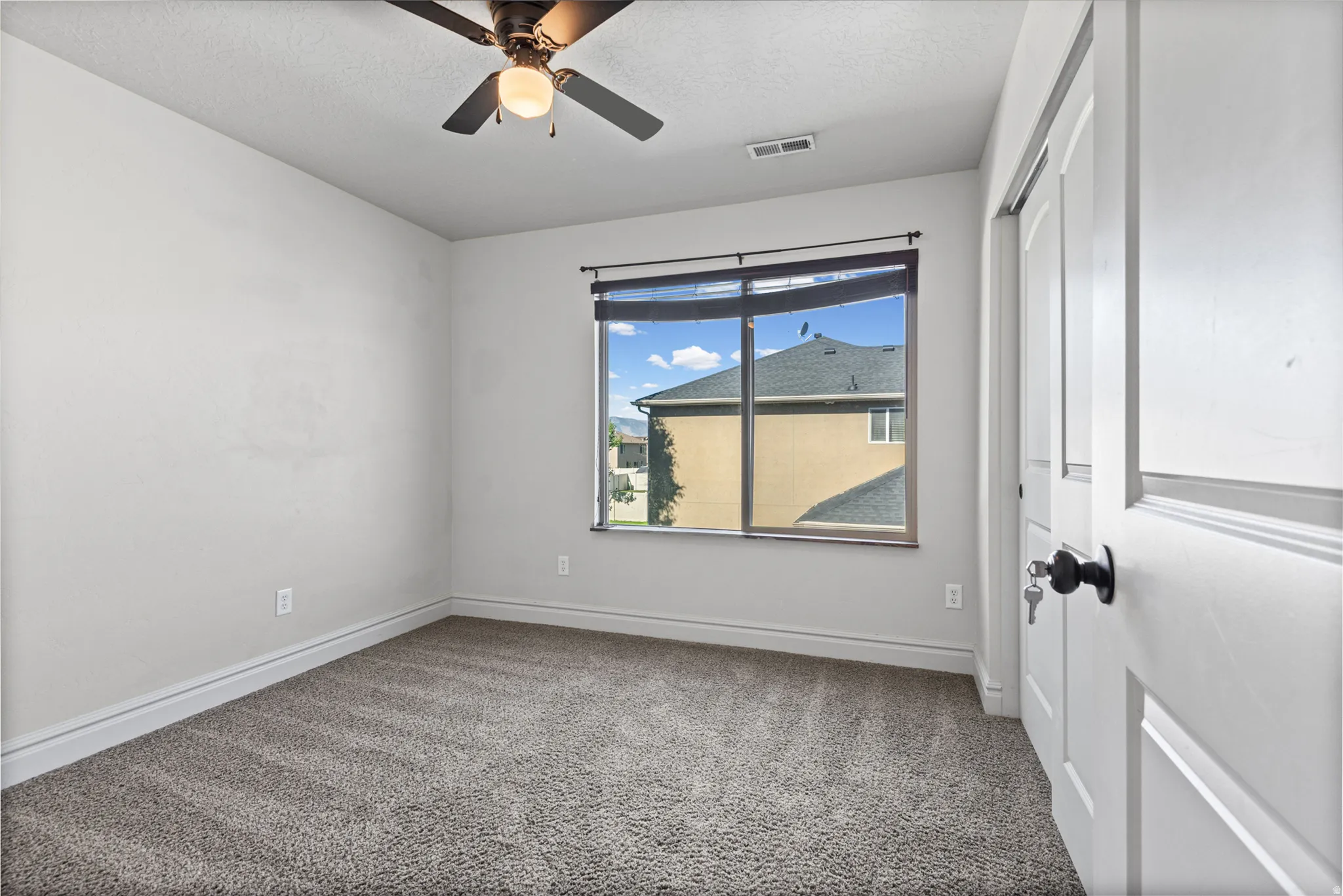 Wall-to-wall carpeting, ceiling fan with integrated lighting, sliding closet doors, and a window with roller shades