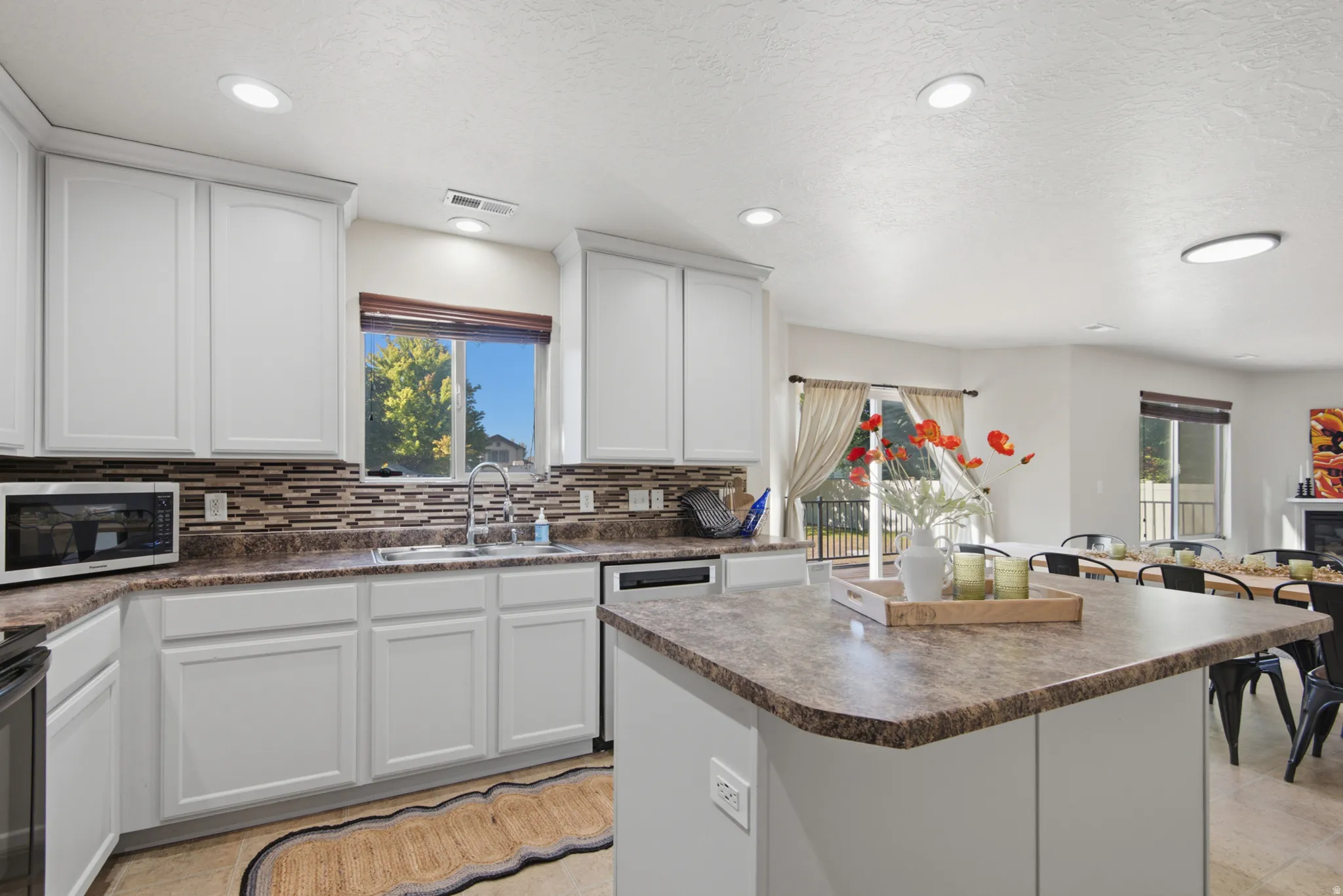 White shaker cabinetry, patterned tile backsplash, recessed ceiling lighting, kitchen island with counter seating, and sliding glass door to exterior