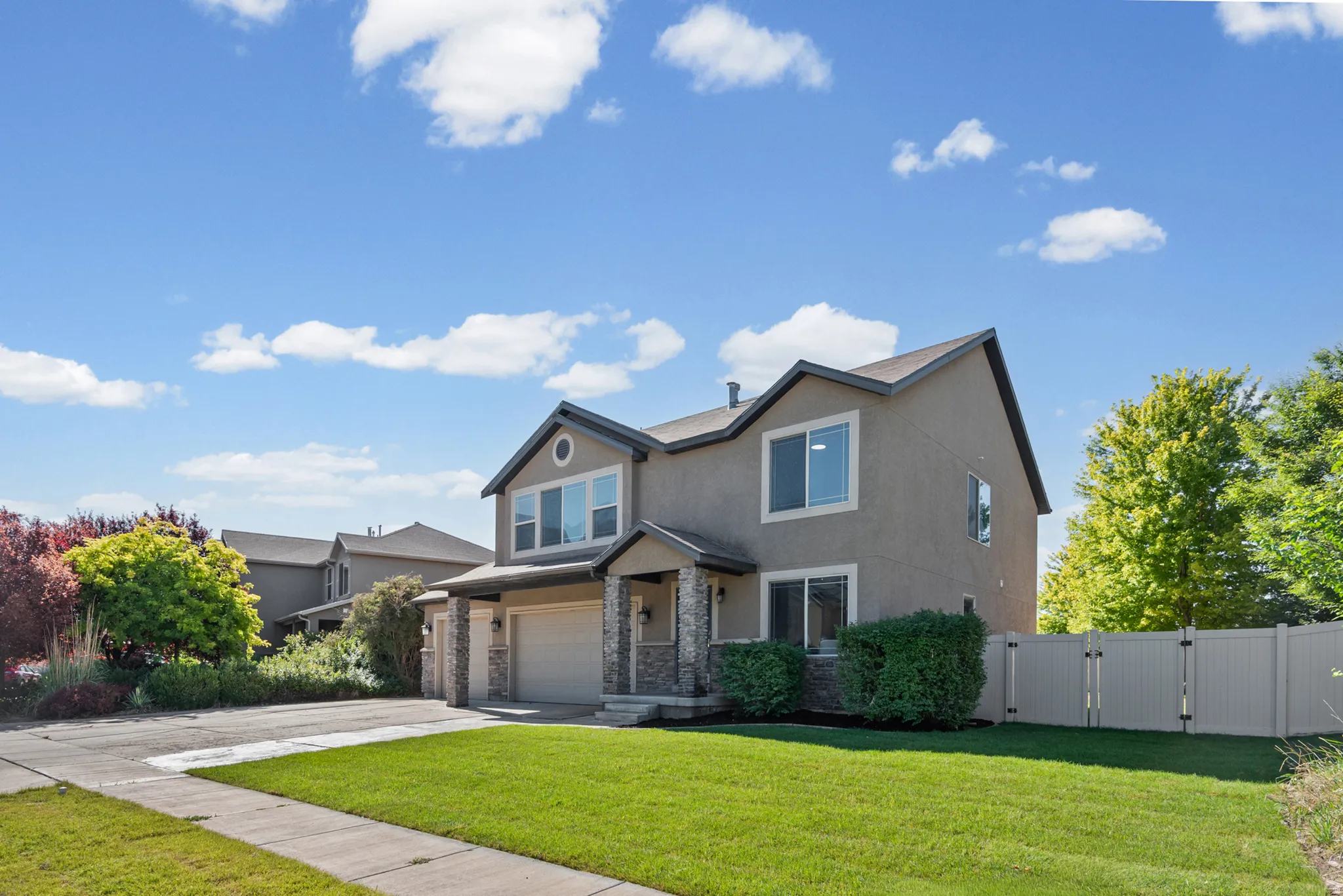 Two-story stucco residence with a pitched roof, stone veneer accents, an attached garage, and a fenced backyard